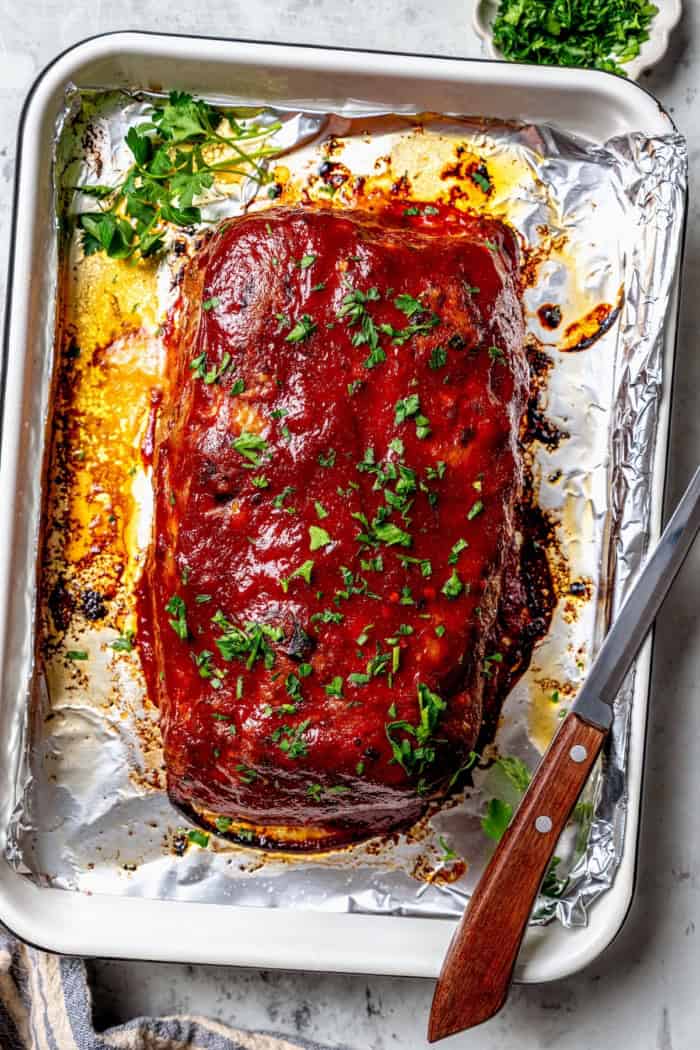 Spicy Meatloaf is a classic with a kick! It has a little Tex-Mex flair thanks to cumin and jalapeño, with a chili glaze to bring the heat. Spicy meatloaf on foil-lined sheet pan with parsley for garnish.