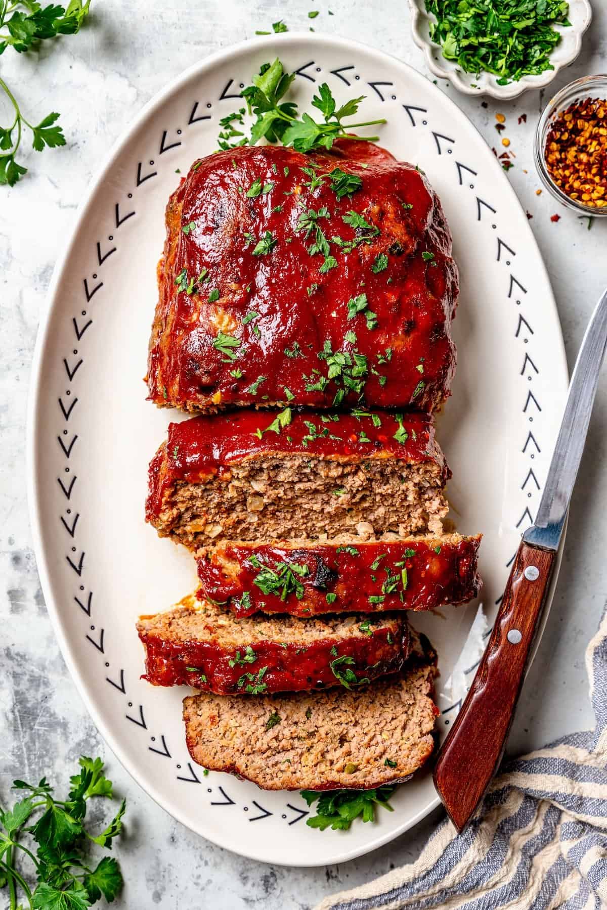Spicy Meatloaf is a classic with a kick! It has a little Tex-Mex flair thanks to cumin and jalapeño, with a chili glaze to bring the heat. Spicy meatloaf on platter with 4 slices cut.