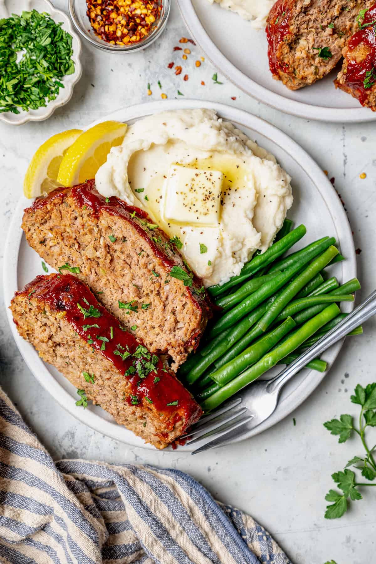 Spicy Meatloaf is a classic with a kick! It has a little Tex-Mex flair thanks to cumin and jalapeño, with a chili glaze to bring the heat. Plate with two spices of spicy meatloaf, green beans, and mashed potatoes.