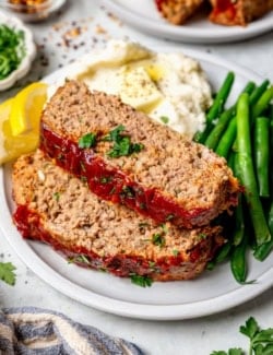 Two slices of spicy meatloaf on plate with mashed potatoes and green beans.