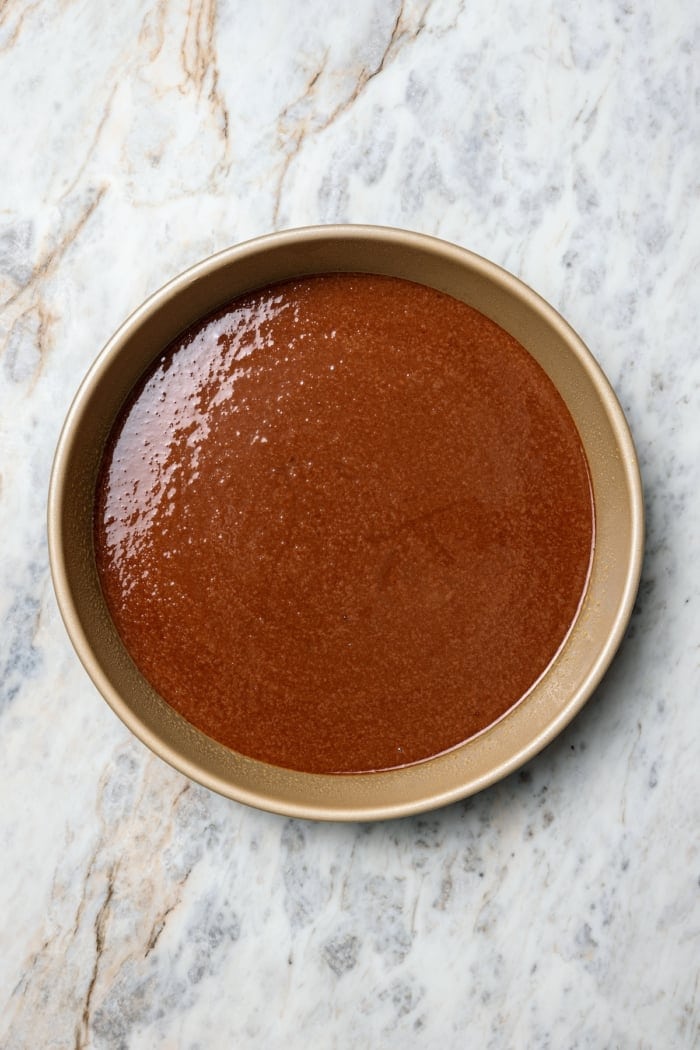 Three layers of dark chocolate cake are smothered with rich fudgy frosting, creamy caramel, and crispy salted pecans. So good! Chocolate cake batter in round pan.