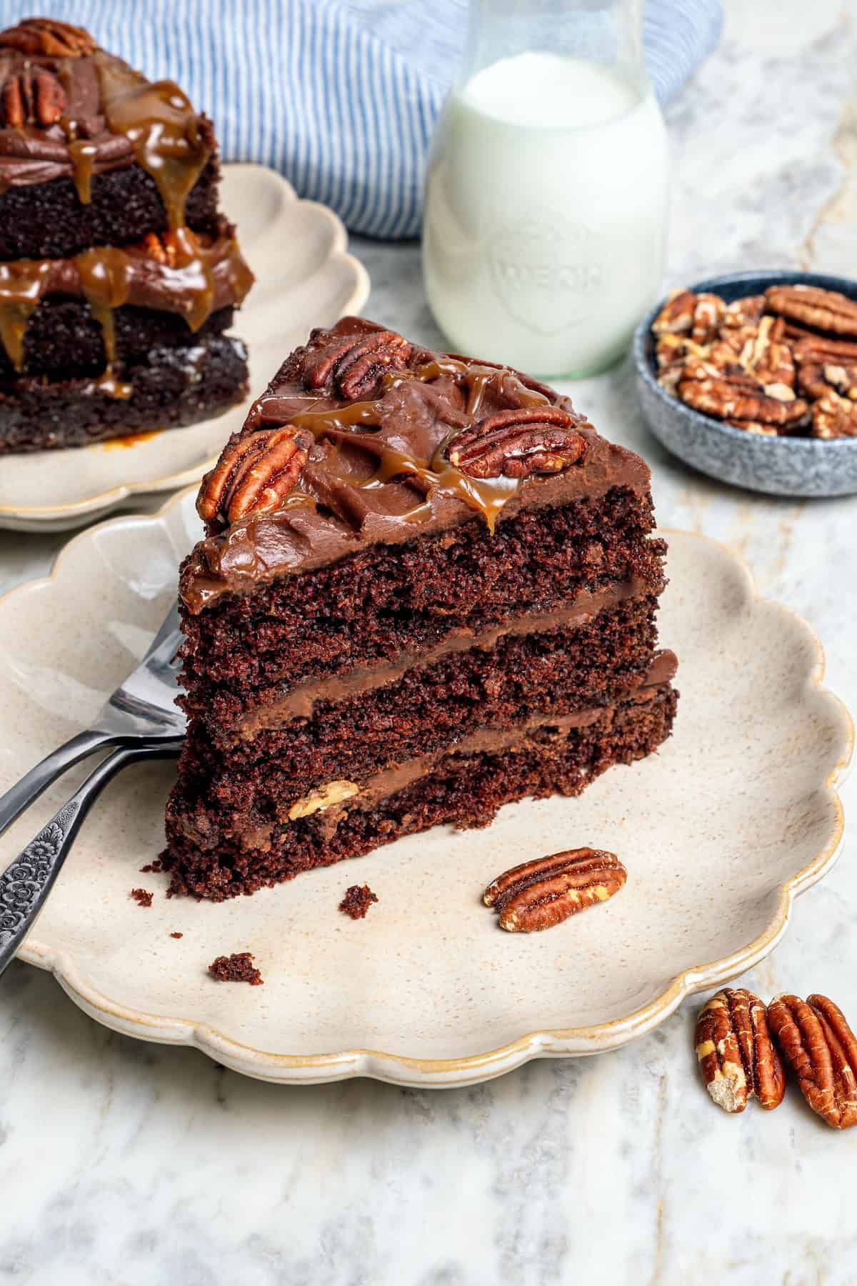 Three layers of dark chocolate cake are smothered with rich fudgy frosting, creamy caramel, and crispy salted pecans. So good! Slice of turtle cake on plate.
