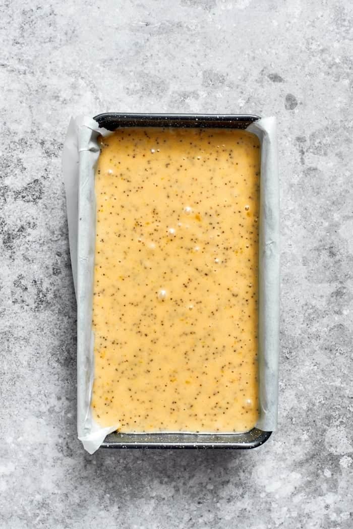 This moist orange poppy seed bread is soaked in a zippy citrus glaze for a bright, tender, bakery-style loaf perfect for brunch or gifting. Orange poppy seed bread batter in pan.