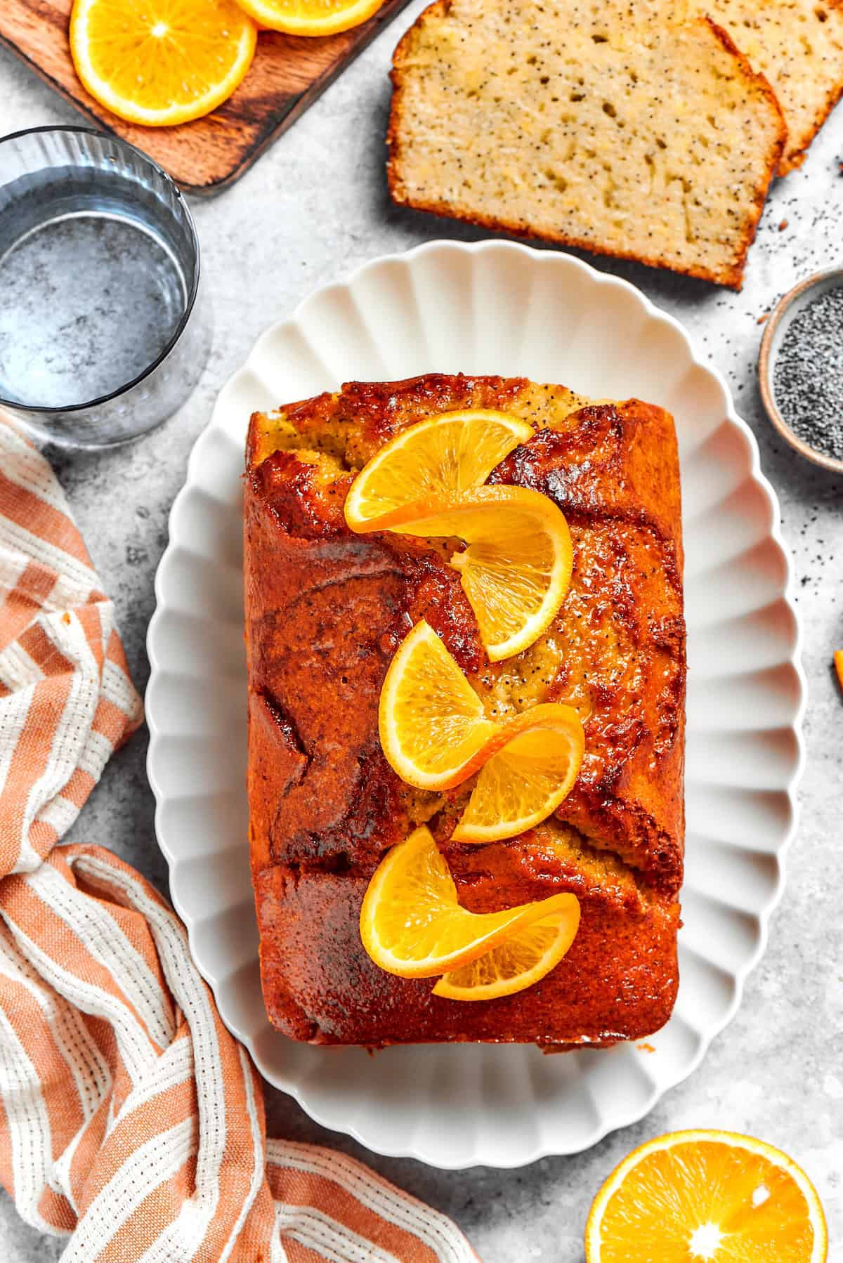 This moist orange poppy seed bread is soaked in a zippy citrus glaze for a bright, tender, bakery-style loaf perfect for brunch or gifting. Loaf of orange glazed poppy seed bread on platter with orange slices on top.