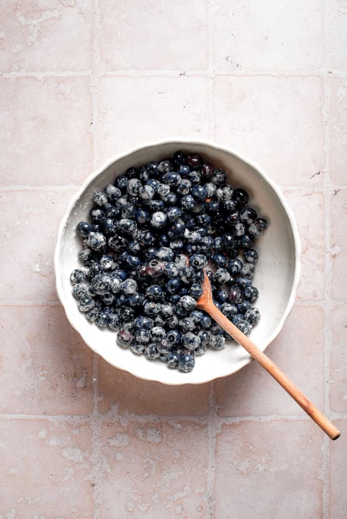 These mini blueberry cobblers are bursting with jammy berries and topped with a buttery, tender, flaky cobbler crust. An easy, rustic dessert! Blueberry filling mixture in bowl with wooden spoon.