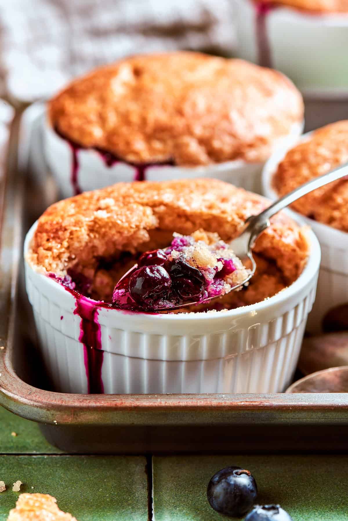 These mini blueberry cobblers are bursting with jammy berries and topped with a buttery, tender, flaky cobbler crust. An easy, rustic dessert! Spoonful of blueberry cobbler in ramekin.