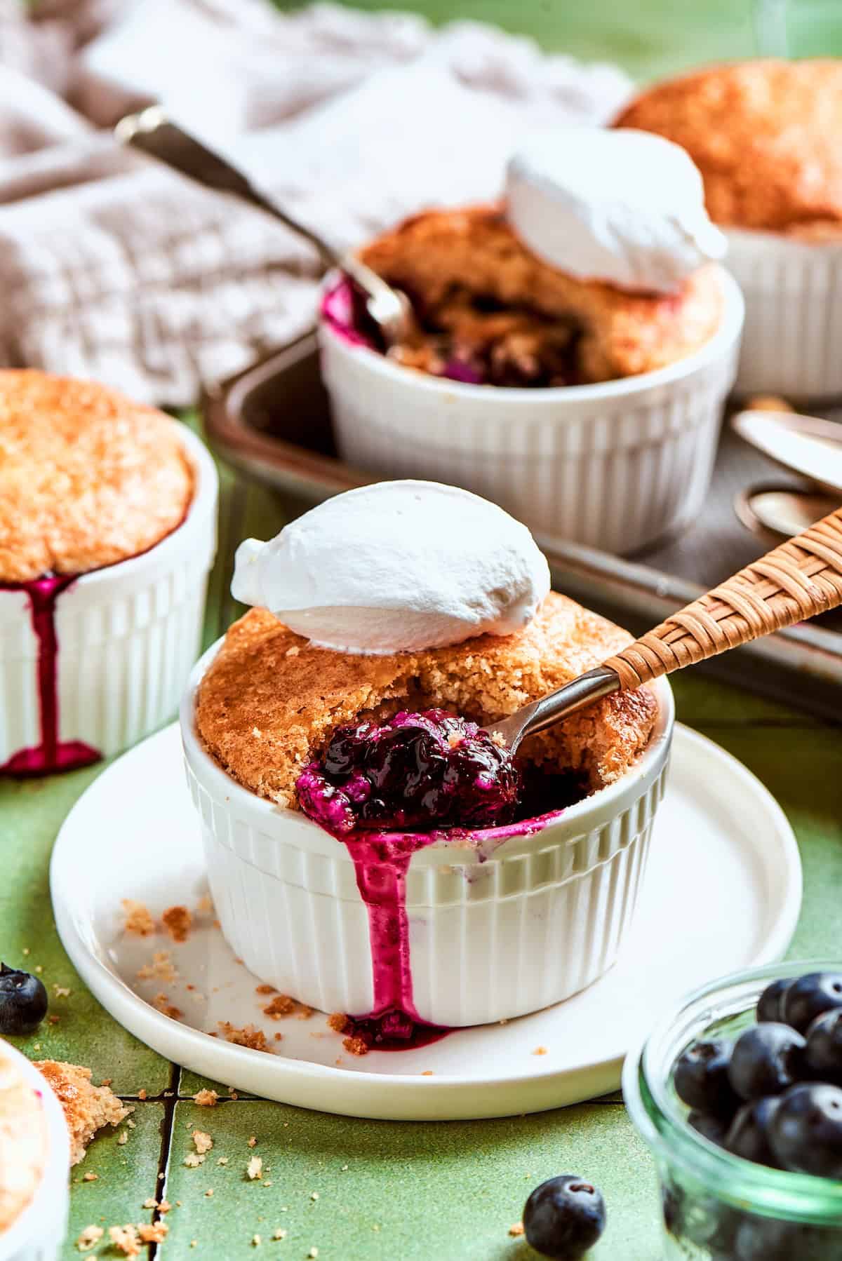 These mini blueberry cobblers are bursting with jammy berries and topped with a buttery, tender, flaky cobbler crust. An easy, rustic dessert! Spoon digging into mini blueberry cobbler topped with scoop of ice cream.