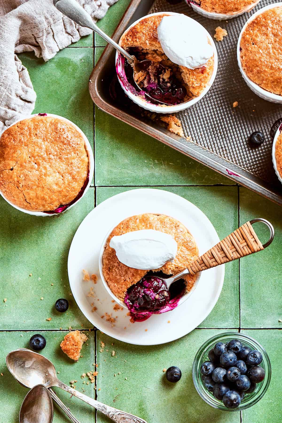 These mini blueberry cobblers are bursting with jammy berries and topped with a buttery, tender, flaky cobbler crust. An easy, rustic dessert! Mini blueberry cobblers on sheet pan, countertop, and plate.