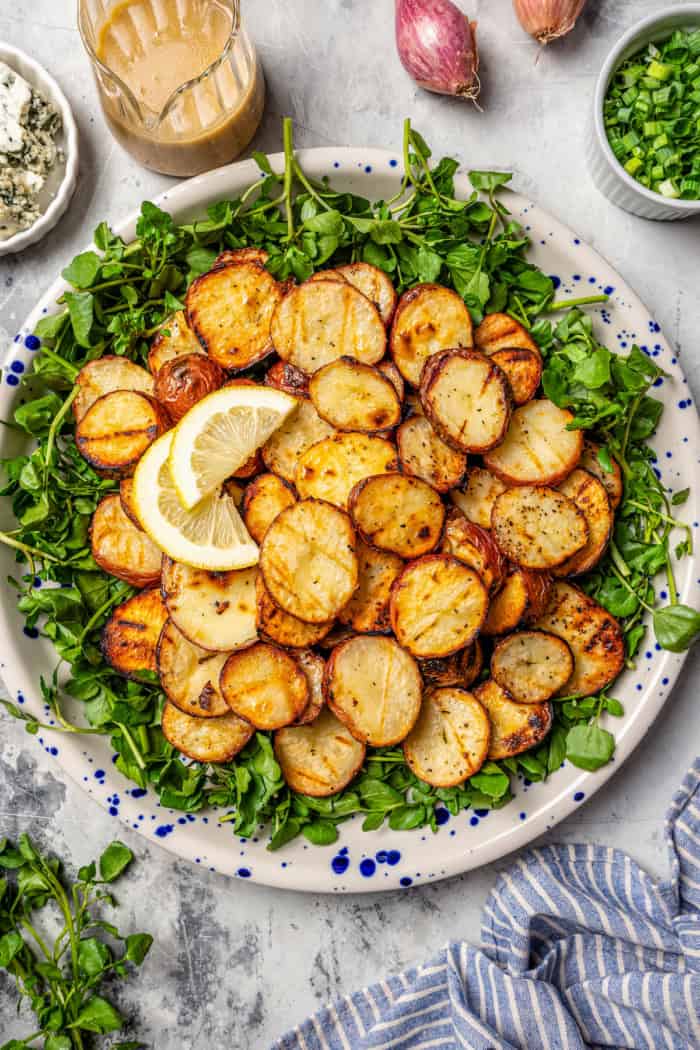 With smoky red potatoes and a rich blue cheese vinaigrette, this grilled potato salad recipe is so delicious, it might just steal the show! Overhead view of grilled potato salad on platter with watercress