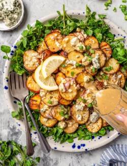 Pouring blue cheese vinaigrette onto platter of grilled potato salad