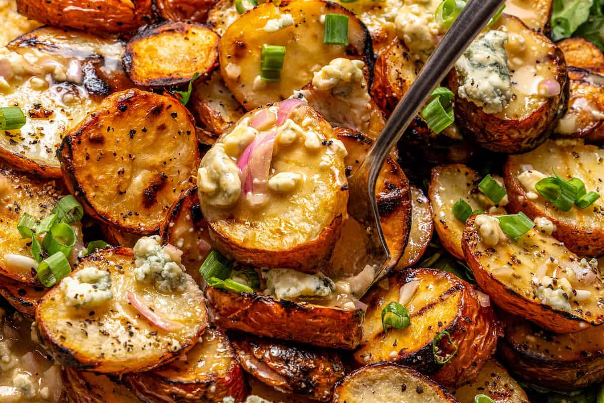 With smoky red potatoes and a rich blue cheese vinaigrette, this grilled potato salad recipe is so delicious, it might just steal the show! Closeup of grilled potato salad with fork digging in