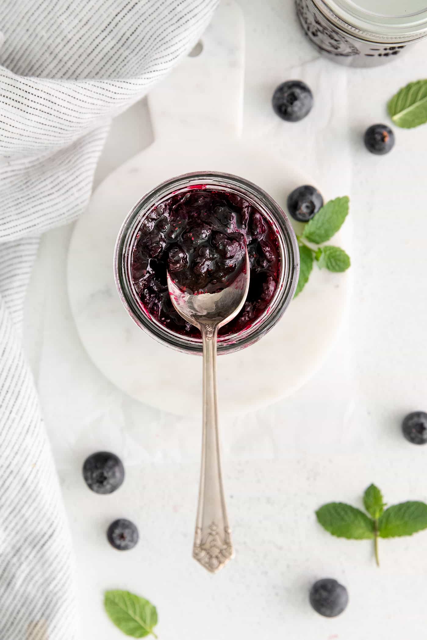 Made with just 4 ingredients, this Homemade Blueberry Jam with Mint is dark and fruity, with a sweet but cool and refreshing flavor. Overhead view of a spoon in a jar of jam