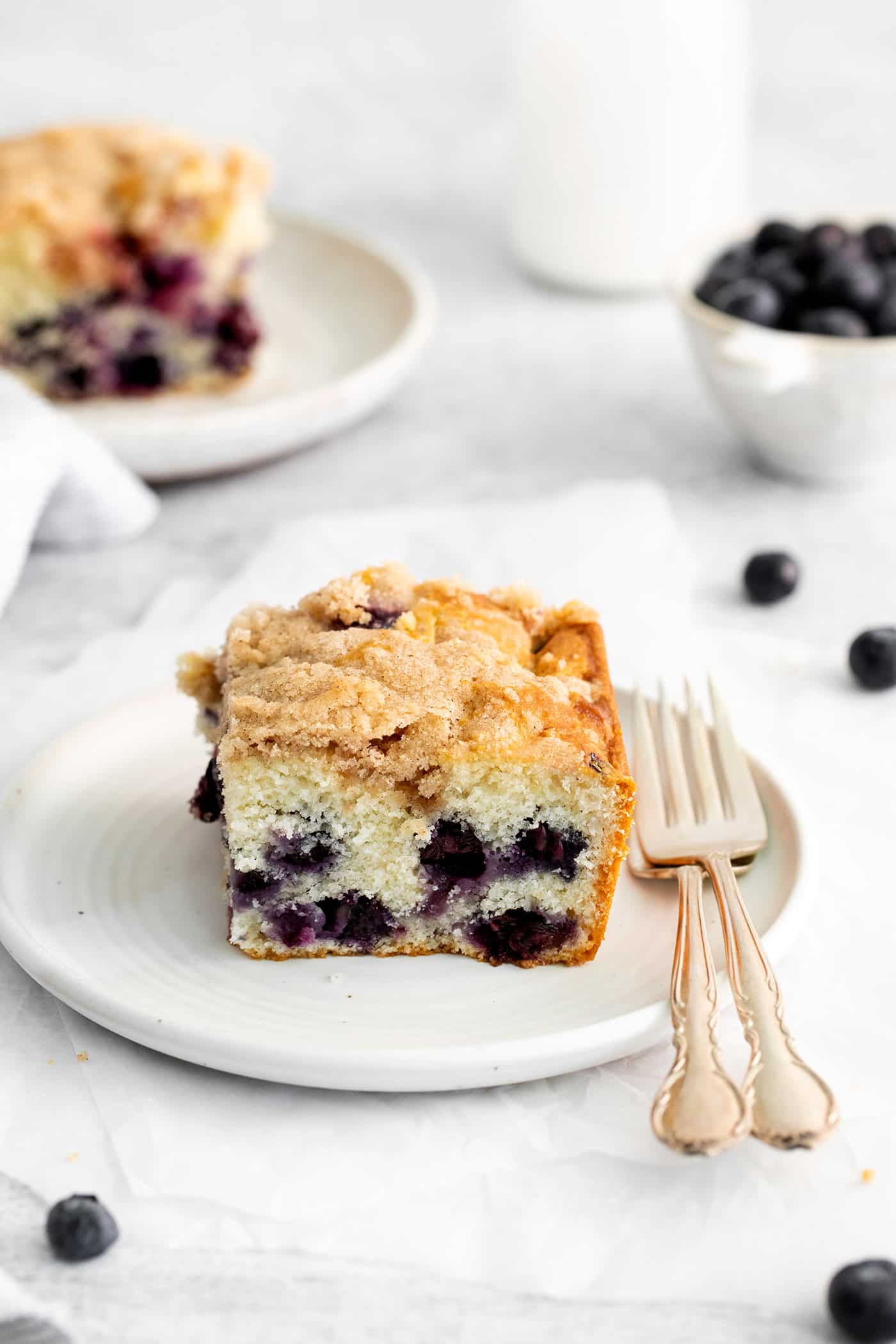 Moist, fluffy, and laced with blueberries in every bite, this Blueberry Tea Cake makes a quick and easy summer dessert. A slice of blueberry cake on a white plate