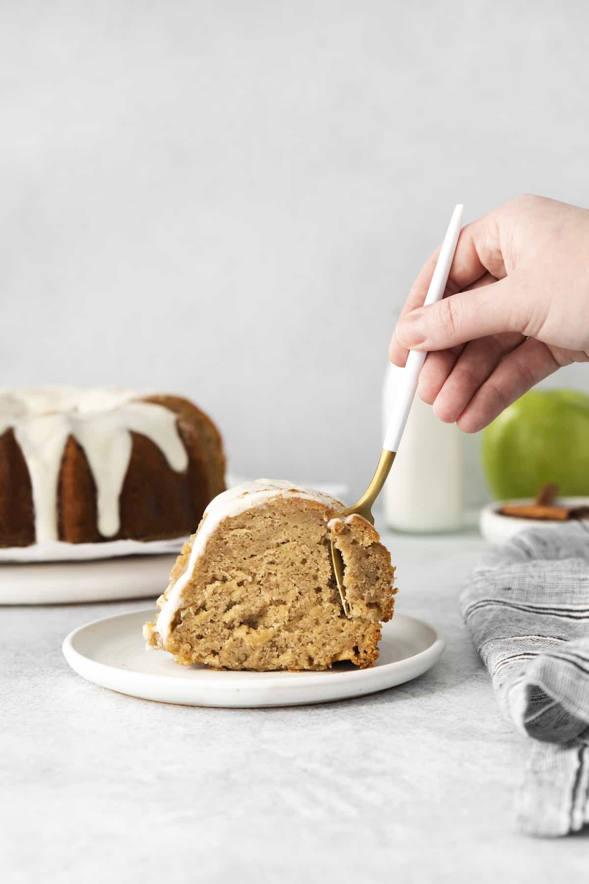 This easy apple bundt cake was made for fall baking! A moist and fluffy apple cake drizzled with an irresistible brown butter vanilla glaze. Hand with a fork, taking a bite out of a slice of apple cake