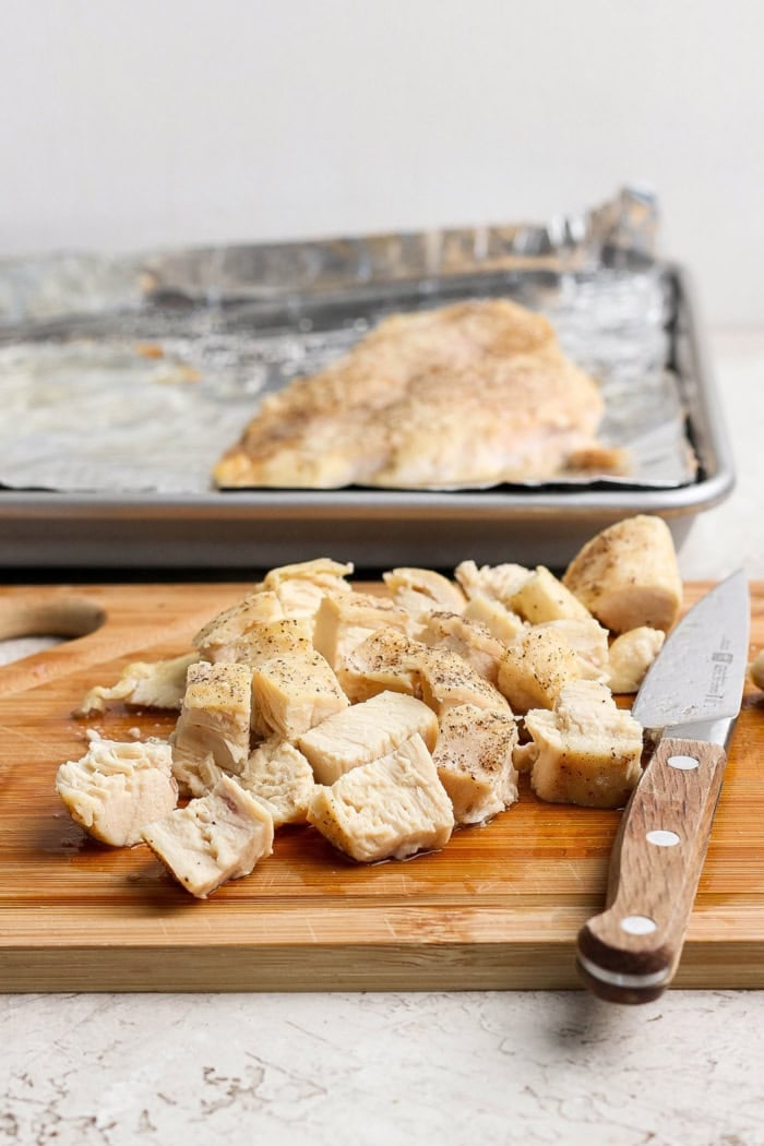 This easy Curry Chicken Salad recipe is the perfect blend of sweet and savory, with juicy grapes, cashews, and a creamy curried dressing. Diced baked chicken on cutting board with knife