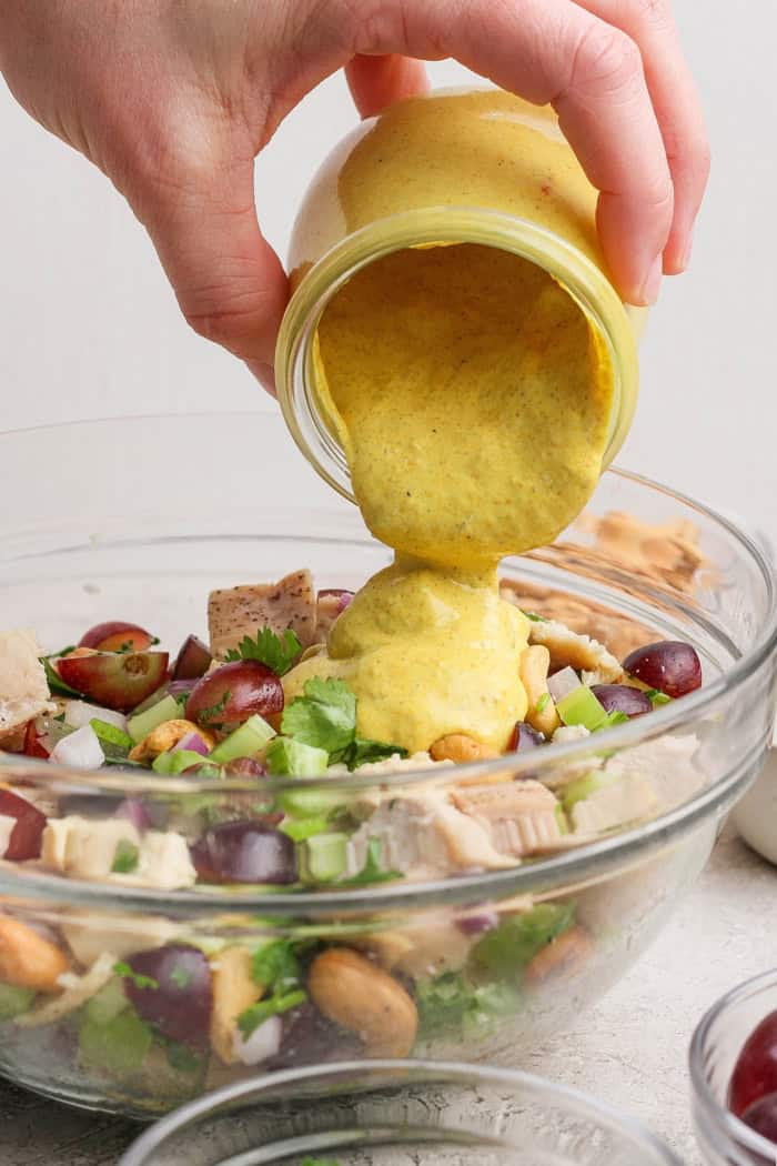 This easy Curry Chicken Salad recipe is the perfect blend of sweet and savory, with juicy grapes, cashews, and a creamy curried dressing. Pouring curry yogurt dressing into bowl of chicken salad