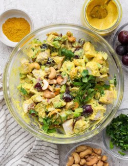 Bowl of curry chicken salad surrounded by smaller bowls of ingredients
