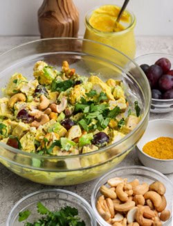 Bowl of curry chicken salad surrounded by smaller bowls of ingredients