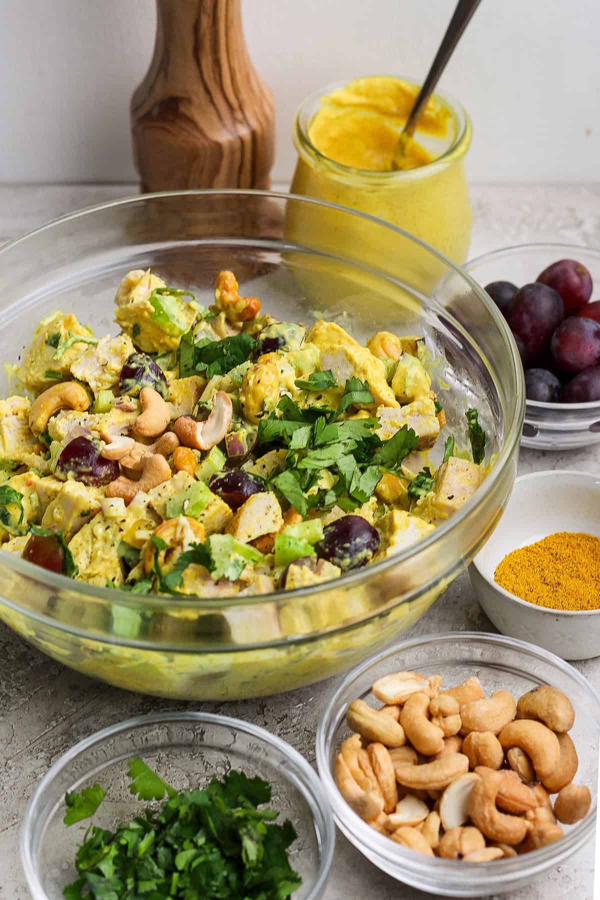 This easy Curry Chicken Salad recipe is the perfect blend of sweet and savory, with juicy grapes, cashews, and a creamy curried dressing. Bowl of curry chicken salad surrounded by smaller bowls of ingredients