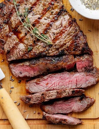 Sliced grilled ribeye steak on cutting board with knife