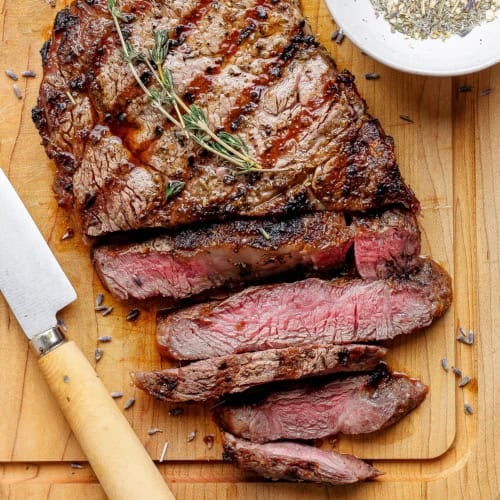 Sliced grilled ribeye steak on cutting board with knife
