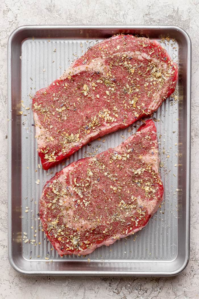 This Grilled Ribeye Recipe will show you the secret to perfectly grilled steak every time! It's tender, juicy, and packed with savory flavor. Two seasoned ribeye steaks before grilling