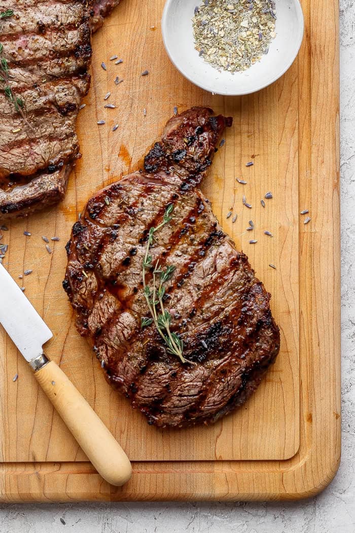 Grilled ribeye steak on cutting board with sprig of thyme.