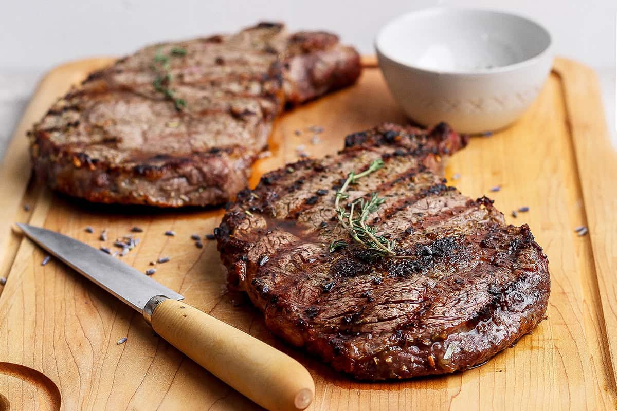 This Grilled Ribeye Recipe will show you the secret to perfectly grilled steak every time! It's tender, juicy, and packed with savory flavor. Two grilled ribeye steaks on cutting board with knife.