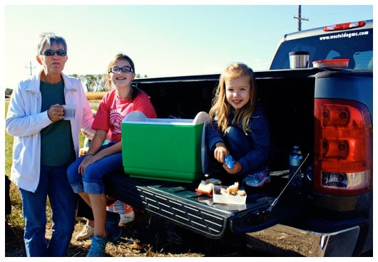Two Girls Sitting on the Back of a Truck With Their Grandma