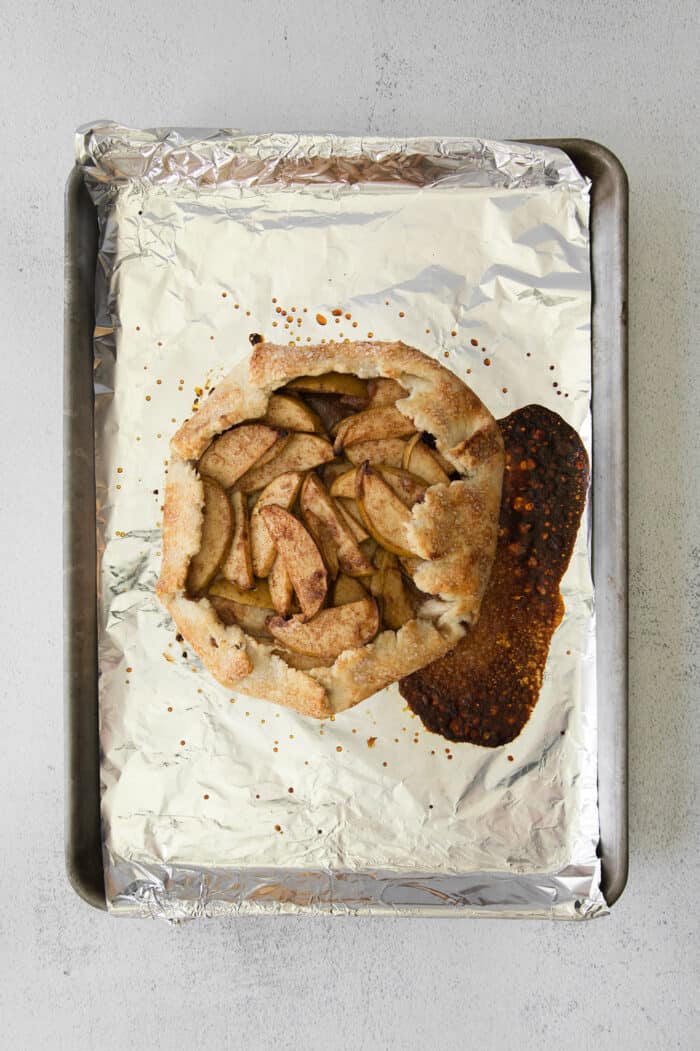 This rustic apple galette has warm cinnamon apples, a buttery crust, and an almond caramel drizzle. It's quicker and easier than apple pie! Baked apple almond galette on foil