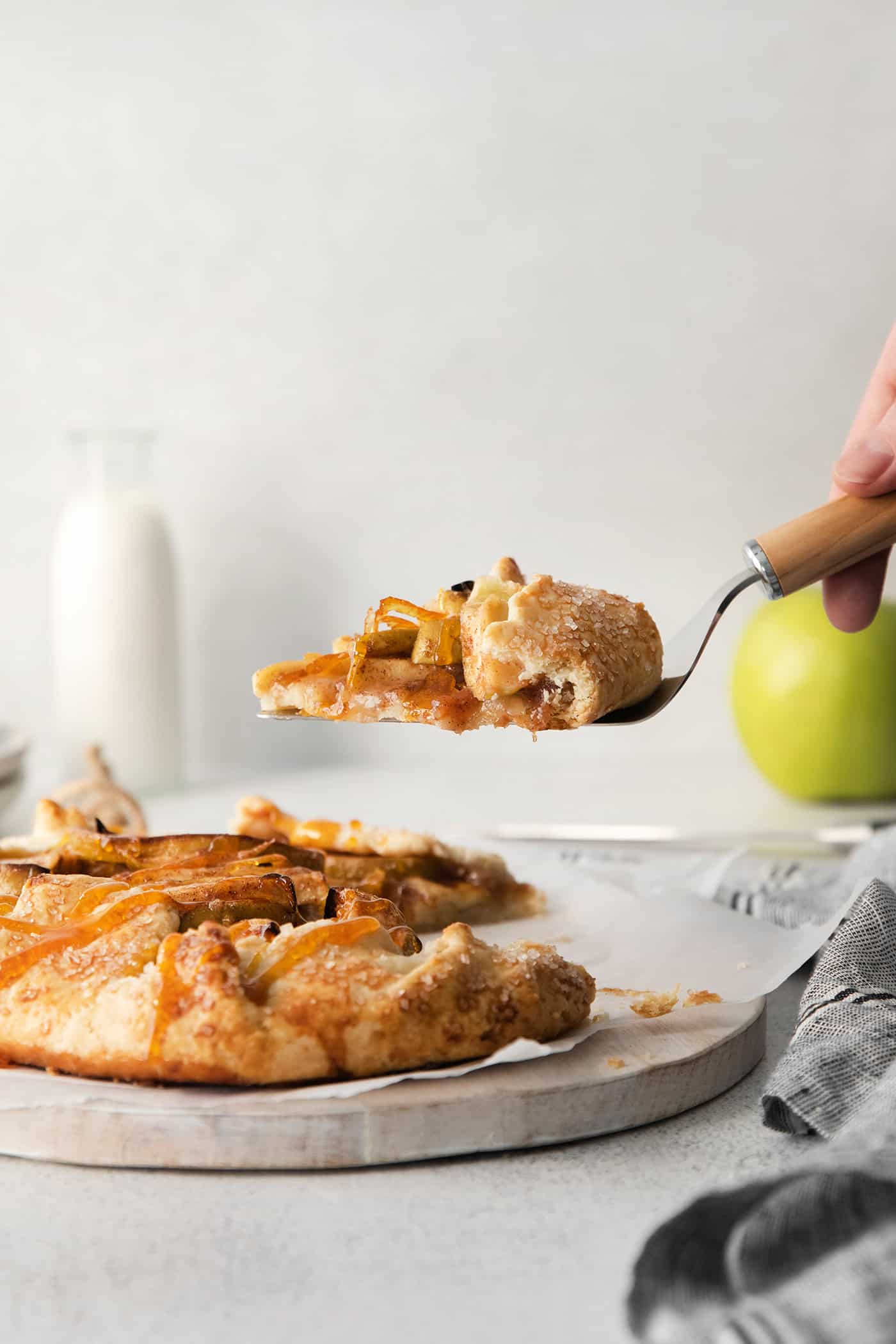 This rustic apple galette has warm cinnamon apples, a buttery crust, and an almond caramel drizzle. It's quicker and easier than apple pie! A slice of apple galette being served