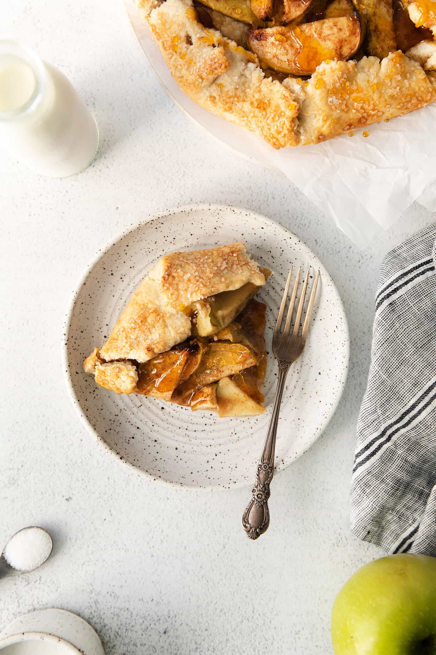 This rustic apple galette has warm cinnamon apples, a buttery crust, and an almond caramel drizzle. It's quicker and easier than apple pie! A slice of apple almond galette on a white plate