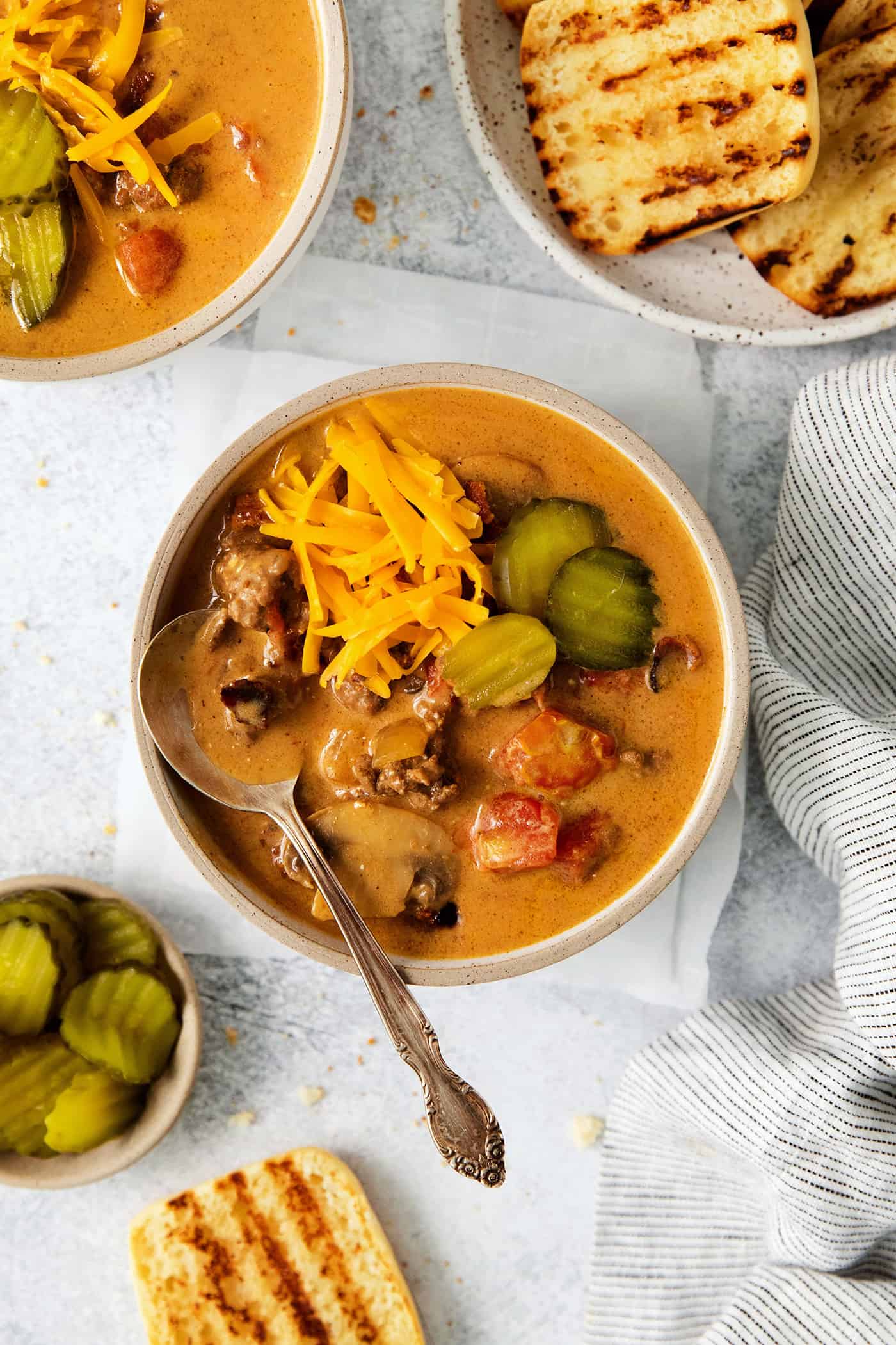 This Bacon Cheeseburger Soup is loaded with your favorite burger ingredients and toppings, like bacon, mushrooms, and a handful of seasonings. Top with shredded cheese and dill pickles for a soup that tastes just like your favorite cheeseburger! Overhead view of a bowl of bacon cheeseburger soup