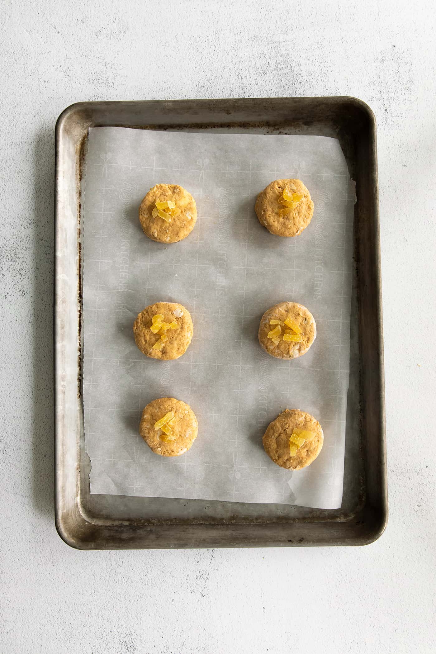 6 rounds of pumpkin biscuit dough topped with candied ginger on a baking sheet