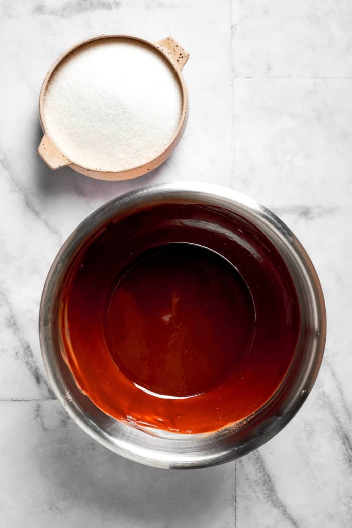 These Red Velvet Brownies are dense and fudgy, exceptionally moist, and fantastically rich. The cream cheese frosting on top is perfection! Overhead view of sugar in bowl with bowl of melted butter and chocolate