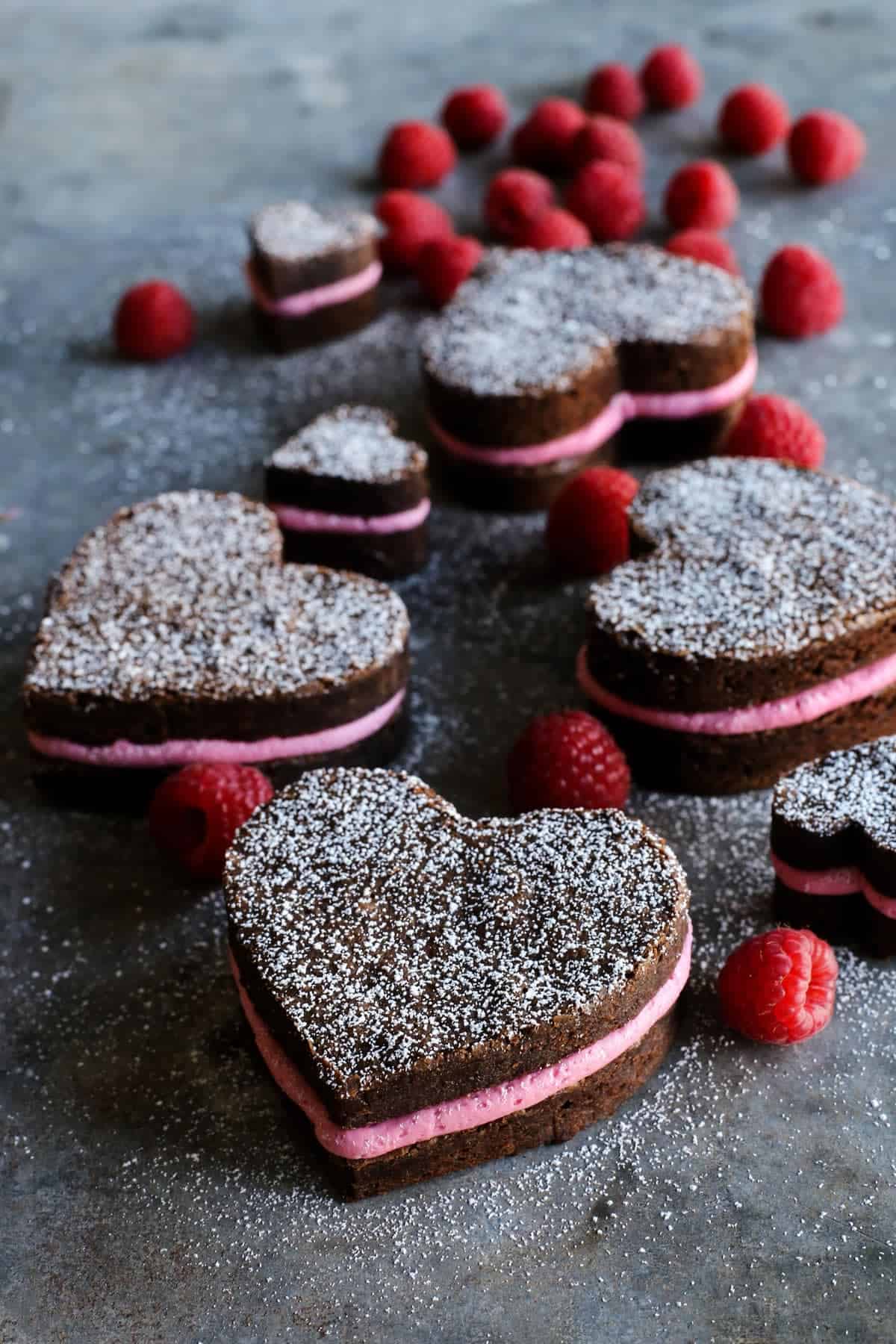 This heart shaped brownies recipe sandwiched with tangy raspberry-lemon buttercream is a super cute, chocolatey Valentine's Day treat. Close-up of heart shaped brownies with raspberry buttercream and a dusting of powdered sugar.