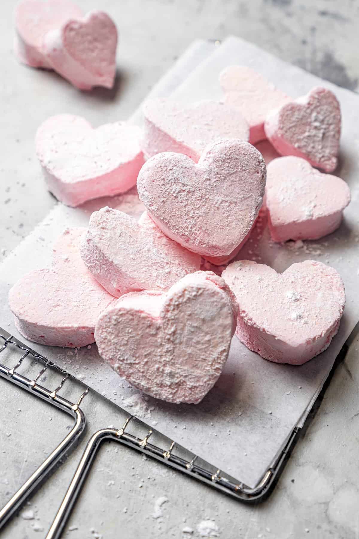 Homemade Marshmallow Hearts are the very best way to send a little love on Valentine’s Day — or any time of year. Fluffy, puffy, and sweet! Pile of fluffy marshmallow hearts on parchment-lined wire rack