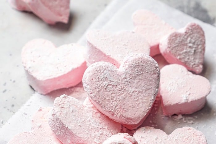 Homemade Marshmallow Hearts are the very best way to send a little love on Valentine’s Day — or any time of year. Fluffy, puffy, and sweet! Pink marshmallow hearts dusted with powdered sugar