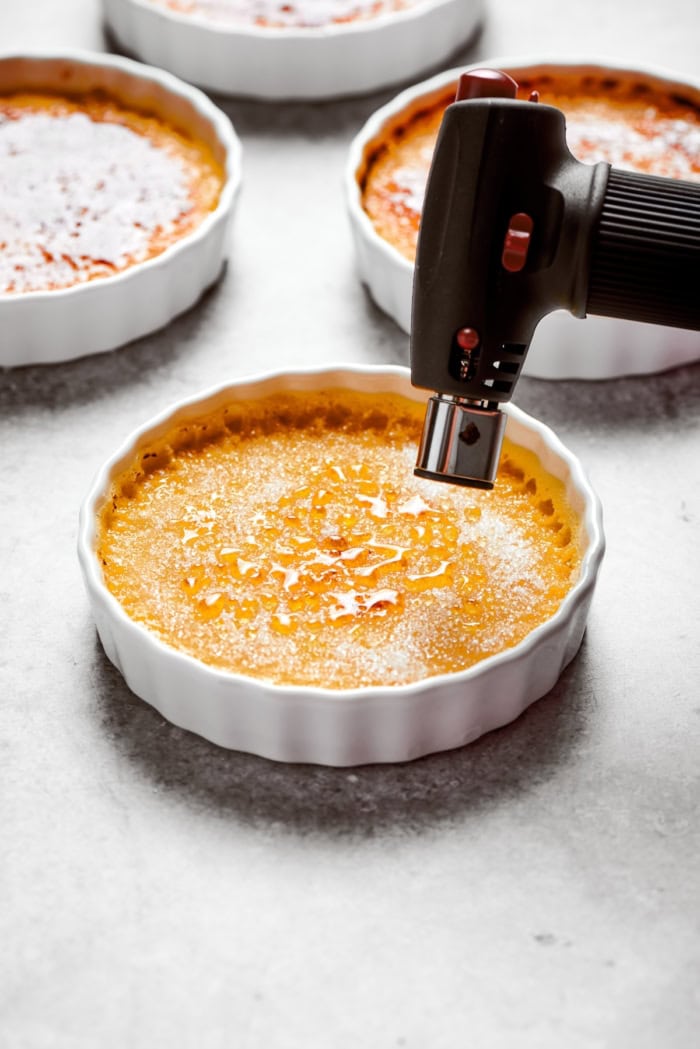 The silky custard in this Almond Vanilla Crème Brûlée lies beneath a glorious caramelized top. An elegant dessert that's surprisingly easy! Kitchen torch caramelizing sugar atop Almond Vanilla Crème Brûlée.