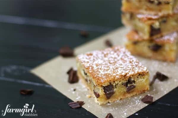 A square of chess pie bar with chocolate chips and powdered sugar on parchment paper