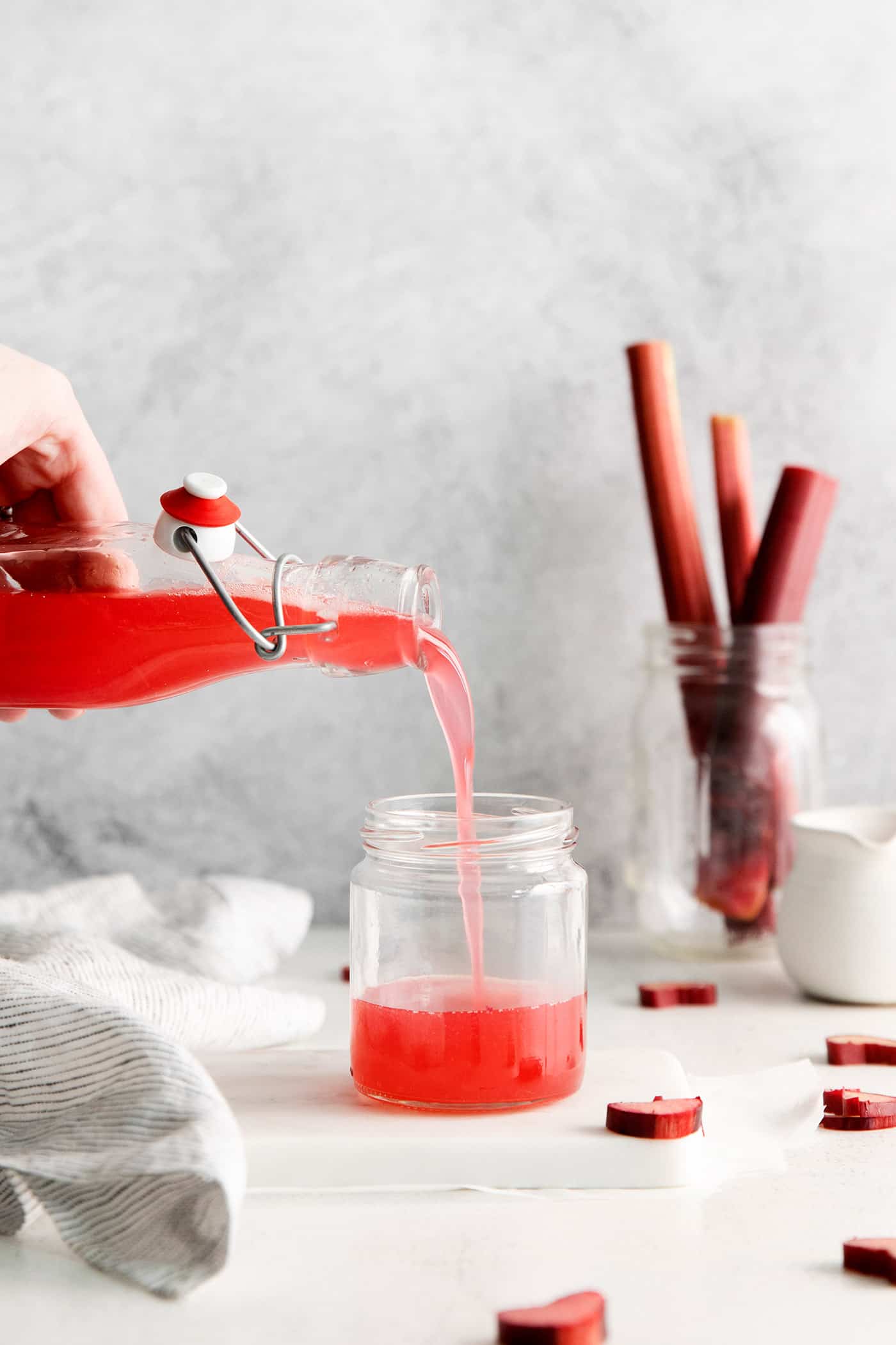 With a sweet-tart flavor, Ruby Rhubarb Syrup is just the thing for the best cocktails and mocktails, not to mention as a topping for pancakes and desserts! Rhubarb syrup being poured into a small jar