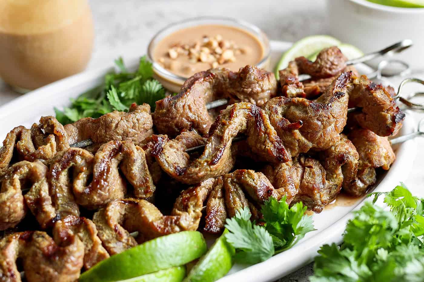 Tender beef is marinated in coconut milk, threaded onto skewers, and grilled to perfection in this coconut beef satay recipe. So flavorful! Coconut beef satay on platter with bowl of peanut sauce