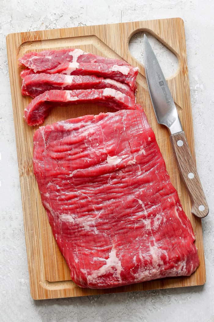 Tender beef is marinated in coconut milk, threaded onto skewers, and grilled to perfection in this coconut beef satay recipe. So flavorful! Beef on wooden cutting board with knife, with 4 slices cut