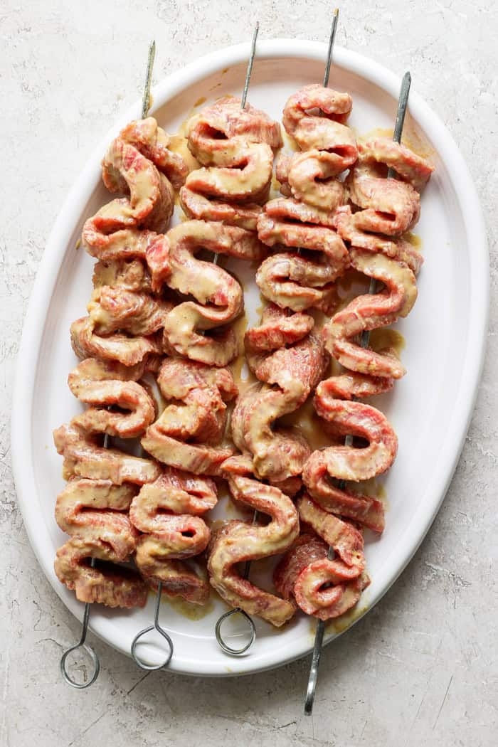 Tender beef is marinated in coconut milk, threaded onto skewers, and grilled to perfection in this coconut beef satay recipe. So flavorful! Overhead view of coconut marinated beef threaded onto skewers for satay