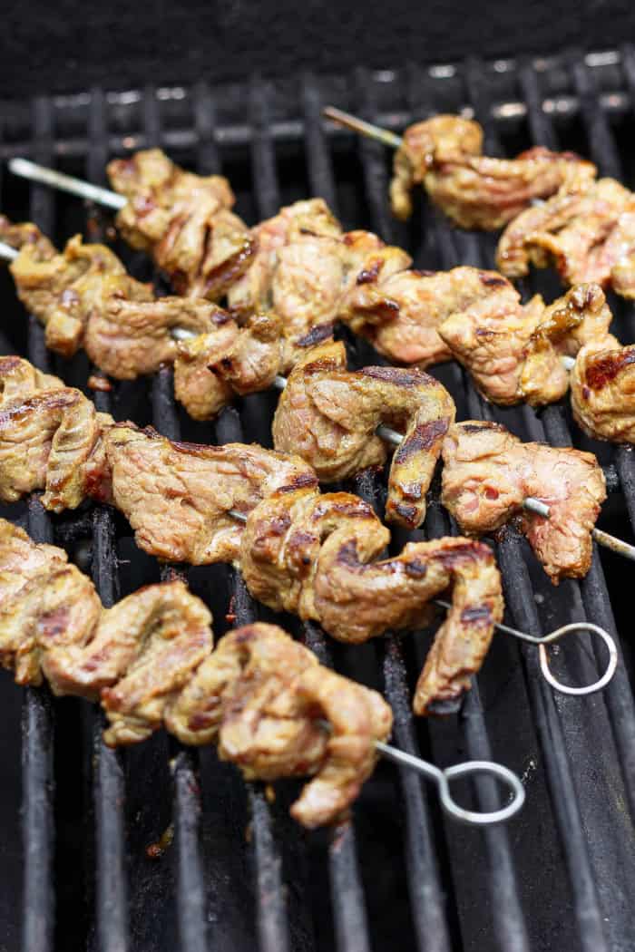 Tender beef is marinated in coconut milk, threaded onto skewers, and grilled to perfection in this coconut beef satay recipe. So flavorful! Coconut beef satay cooking on grill