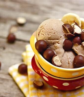 A bowl of chocolate ice cream with malted balls and banana slices