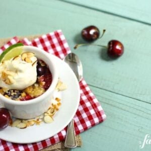 a white ramekin with cherry crumble and whipped cream