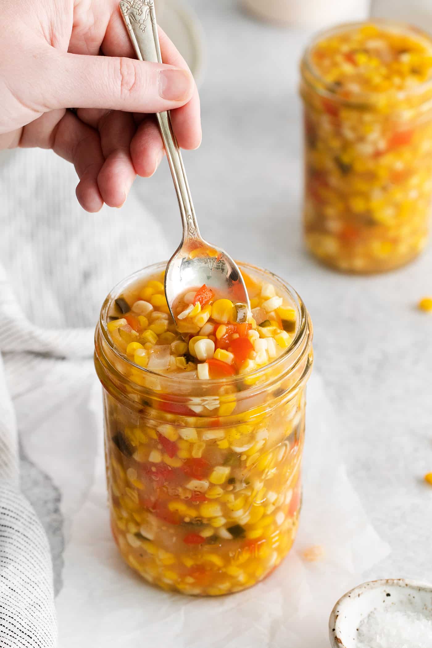 Made with fresh sweet corn, peppers, and onion this Zesty Sweet Corn Relish is just what you need to spice up dishes from tacos to burgers. A spoon stirring a jar of sweet corn relish
