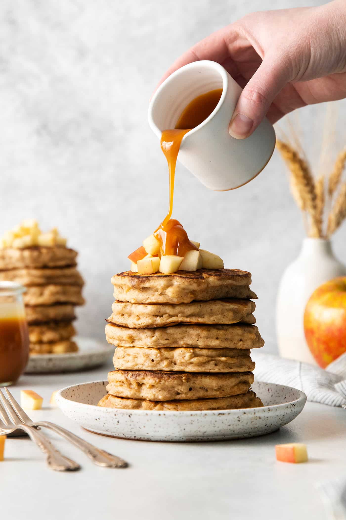Studded with bits of apple and oats, these Apple Oatmeal Pancakes are a cozy, comforting breakfast that's hearty yet not heavy. Caramel buttermilk syrup being poured over a stack of pancakes