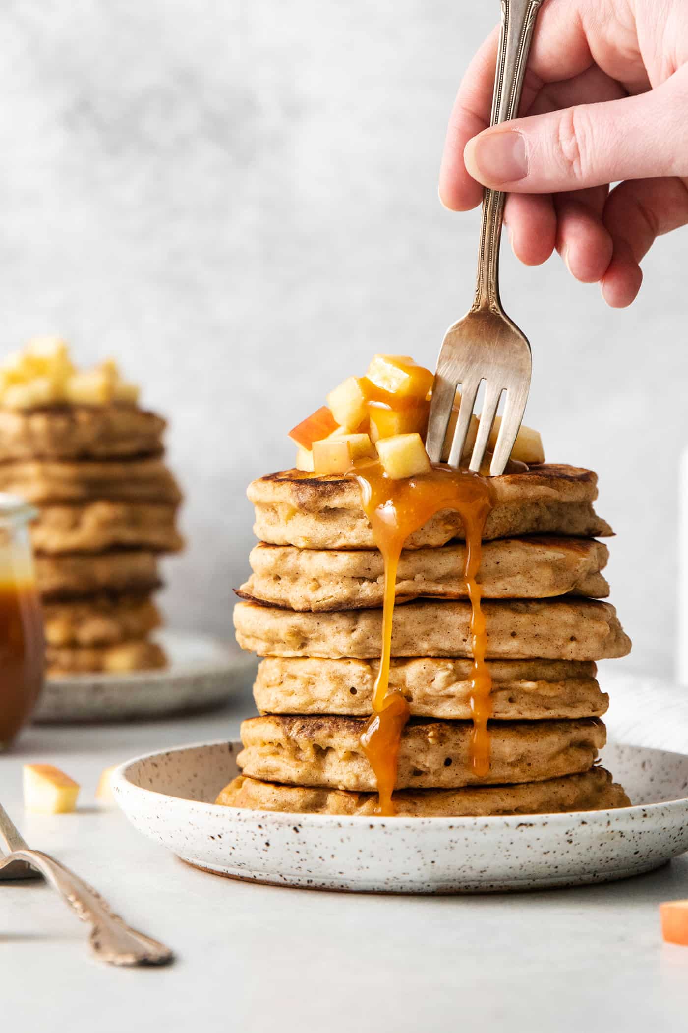 Studded with bits of apple and oats, these Apple Oatmeal Pancakes are a cozy, comforting breakfast that's hearty yet not heavy. A fork diving into a stack of apple oat pancakes